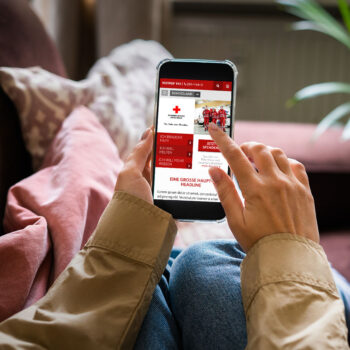 Hände halten Smartphone und Screen zeigt Roteskreuz Startseite