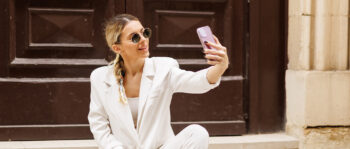 Frau in weißem Hosenanzug und Brille macht ein Selfie