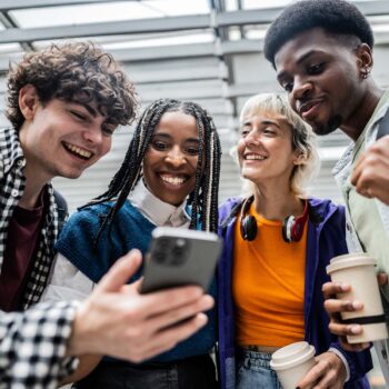 Vier junge Menschen schauen auf ein Smartphone und lachen